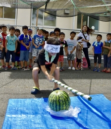 男の子がスイカを割ろうとしているのを、たくさんの子どもたちが応援している写真