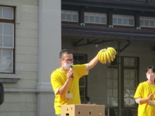 バナナを左手で高くあげながらバナナのたたき売りをする男性