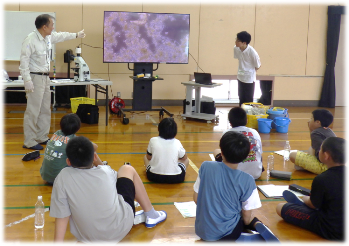 顕微鏡で見る下水をきれいにする生き物に興味津々な子どもたちの写真